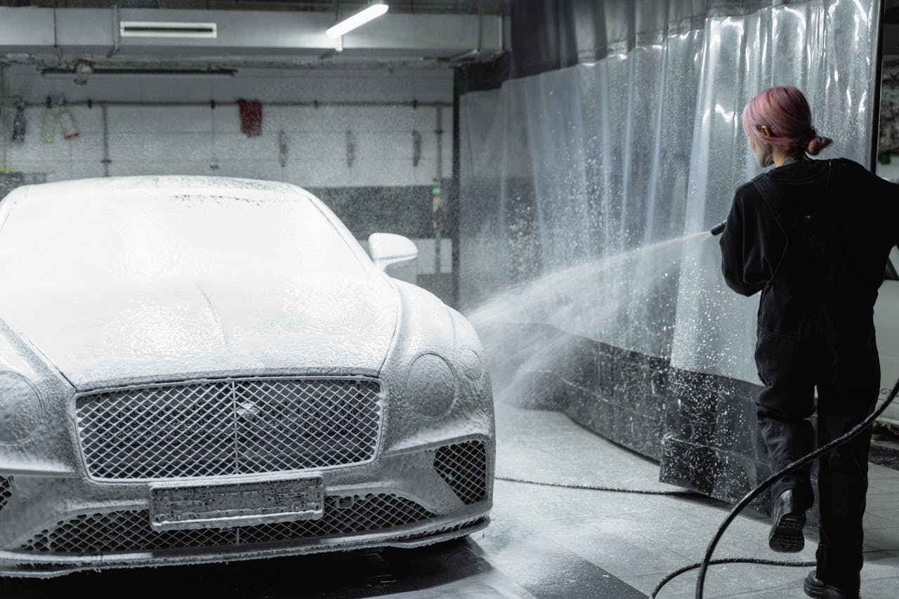 A woman uses a pressure washer to clean a car in an indoor garage, showcasing professional car washing.
